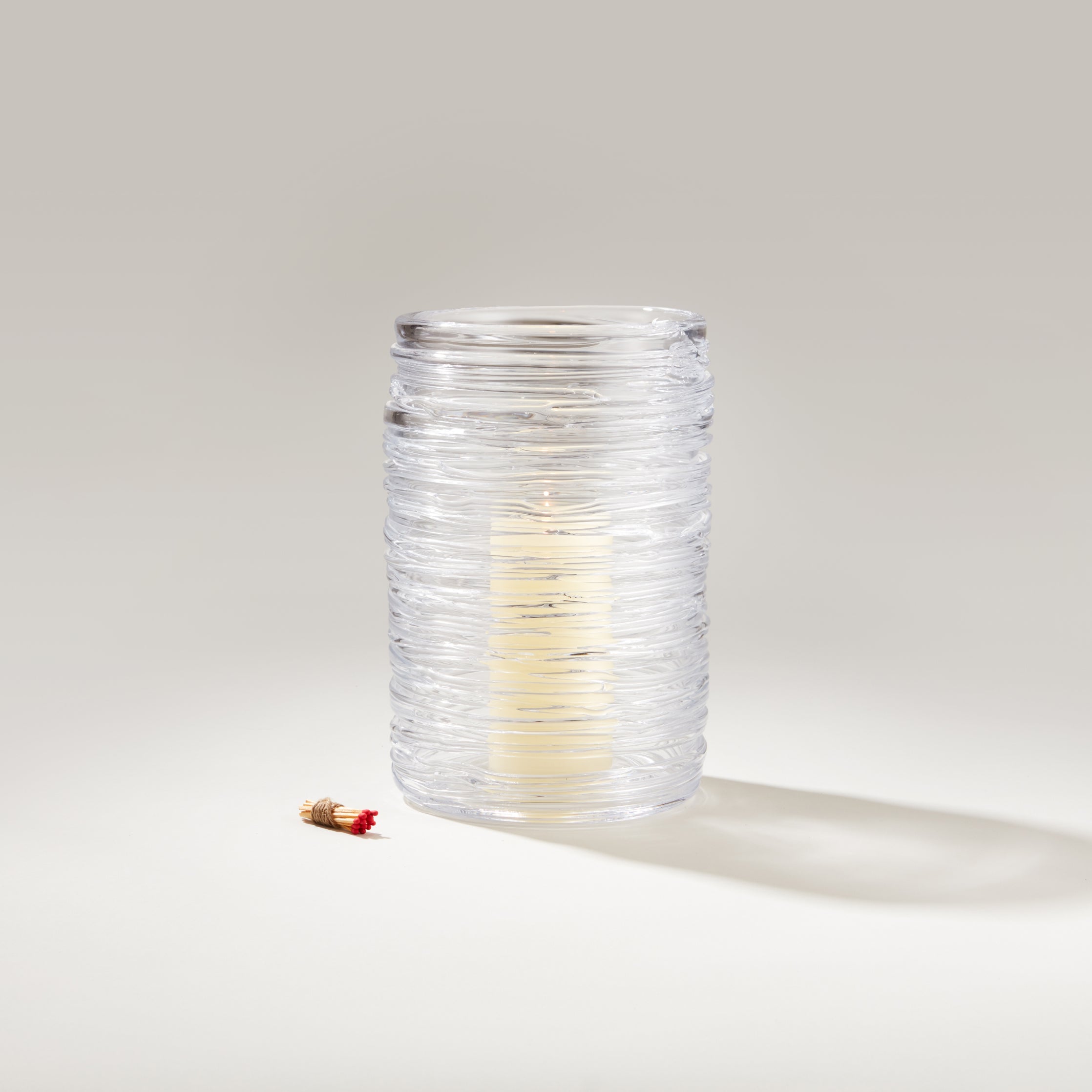 Candles in glass holders on a wooden table in a lush garden setting.