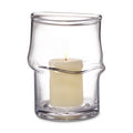 Clear glass hurricane with twisted design holding a lit cream-colored pillar candle.