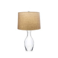 Clear glass bottle-shaped base with tan linen cylindrical shade and metal top finial.