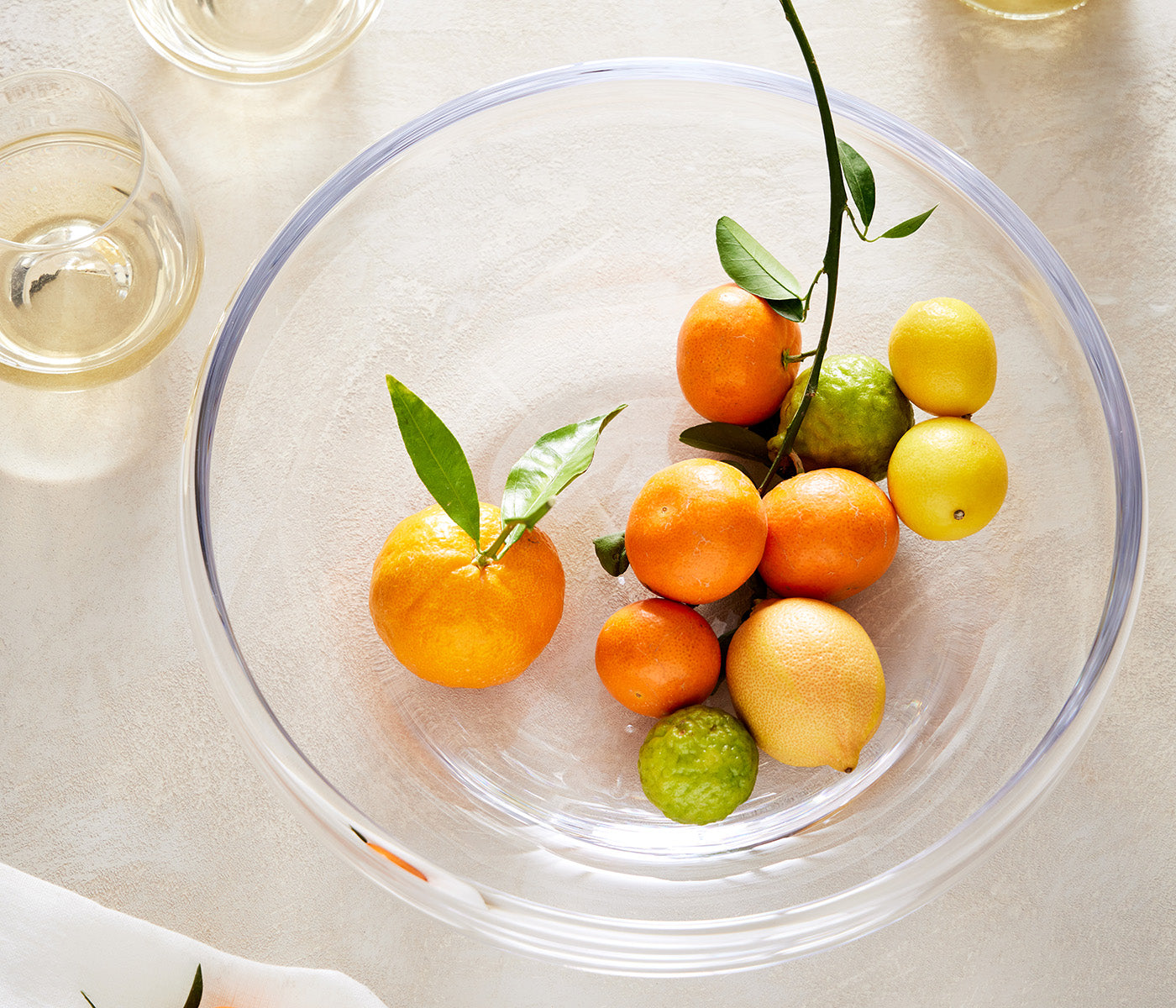 Clear glass platter with purple rim holding assorted citrus fruits with leaves and stems.