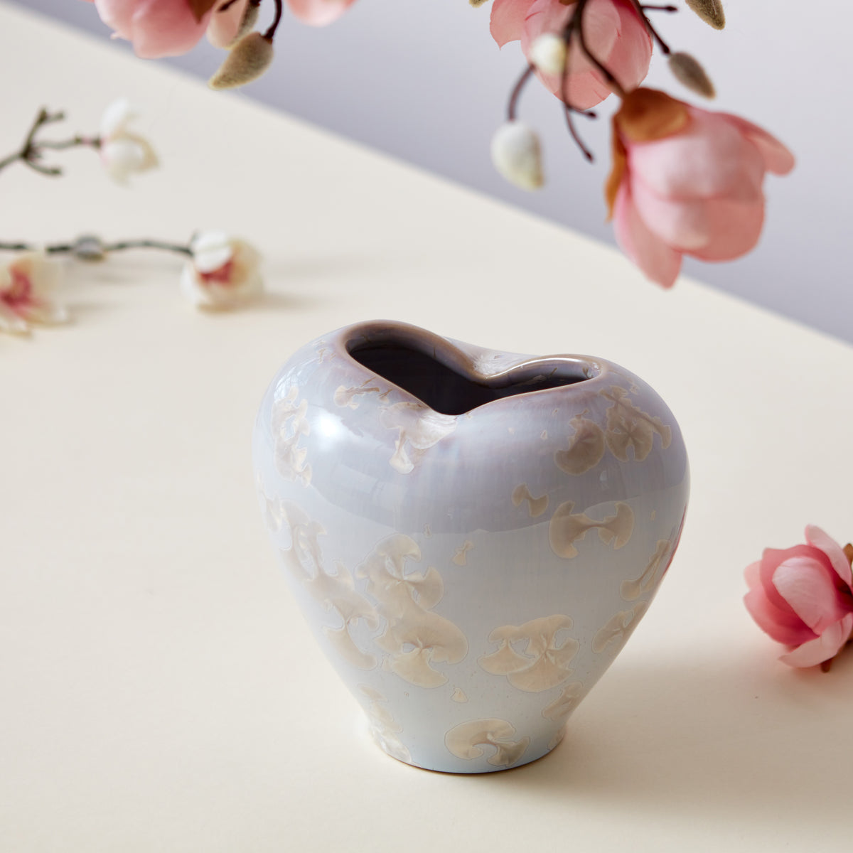 White heart-shaped ceramic vase with embossed floral pattern and curved opening, displayed with pink flowers.