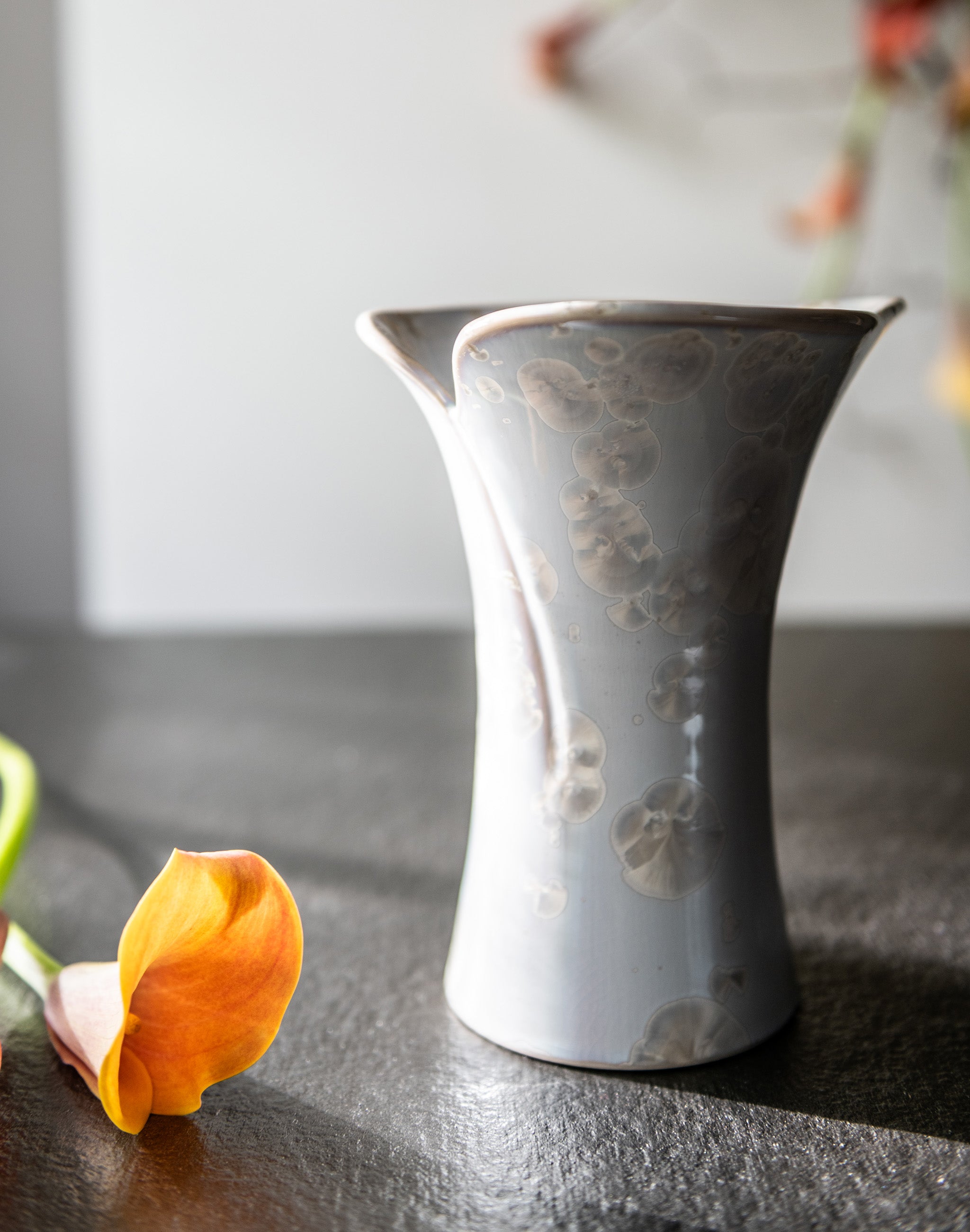 White ceramic vase with floral etched pattern and flared calla lily-shaped opening, displayed with orange flower.