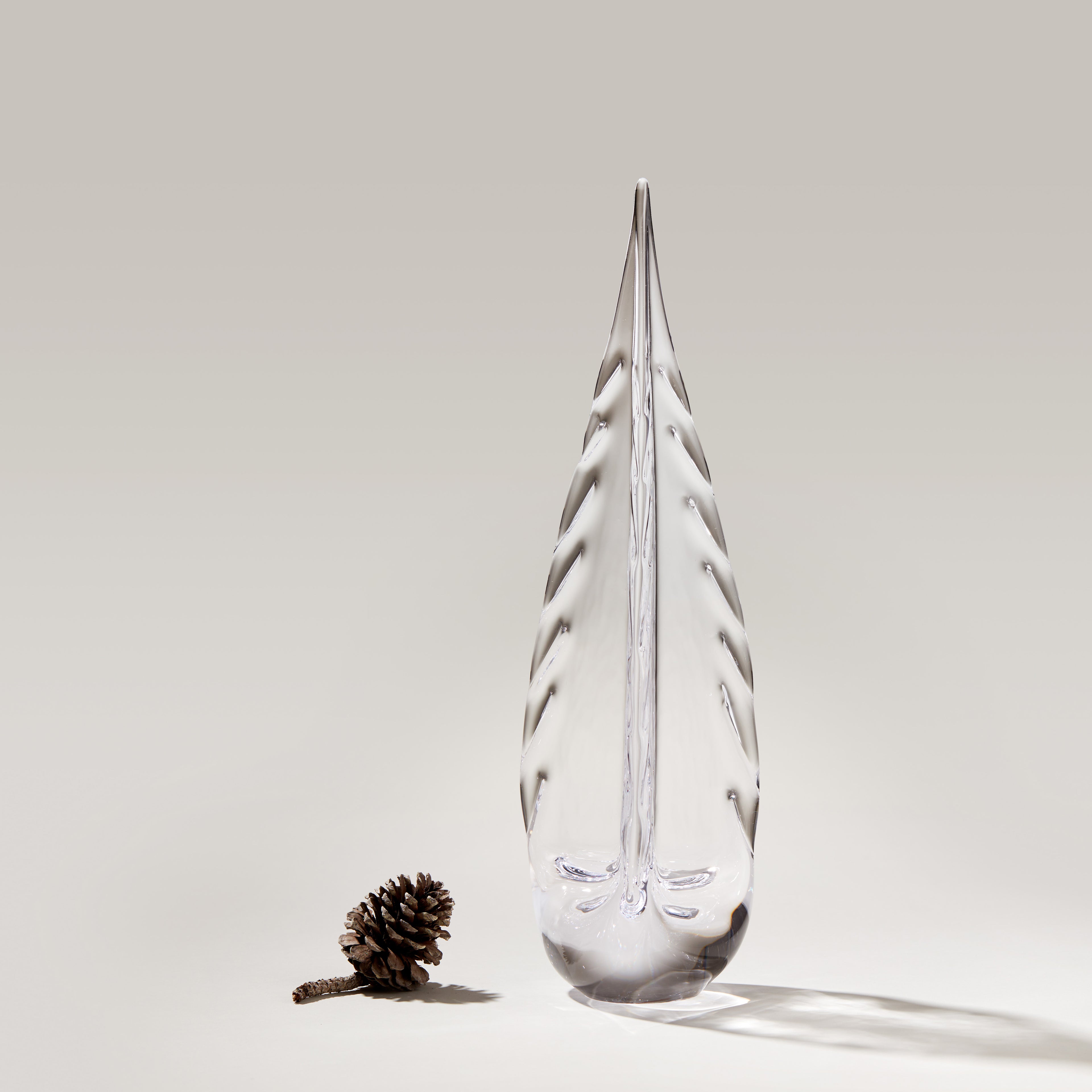 Clear teardrop-shaped glass ornament with frosted evergreen tree design and pinecone beside it.