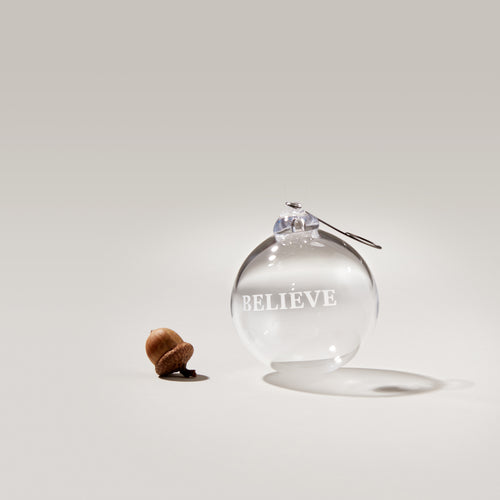 Clear glass round ornament with "BELIEVE" engraved on surface and metal hanging hook.