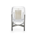 Clear glass hurricane with cream pillar candle inside, supported by stainless steel stand with cross-base design.