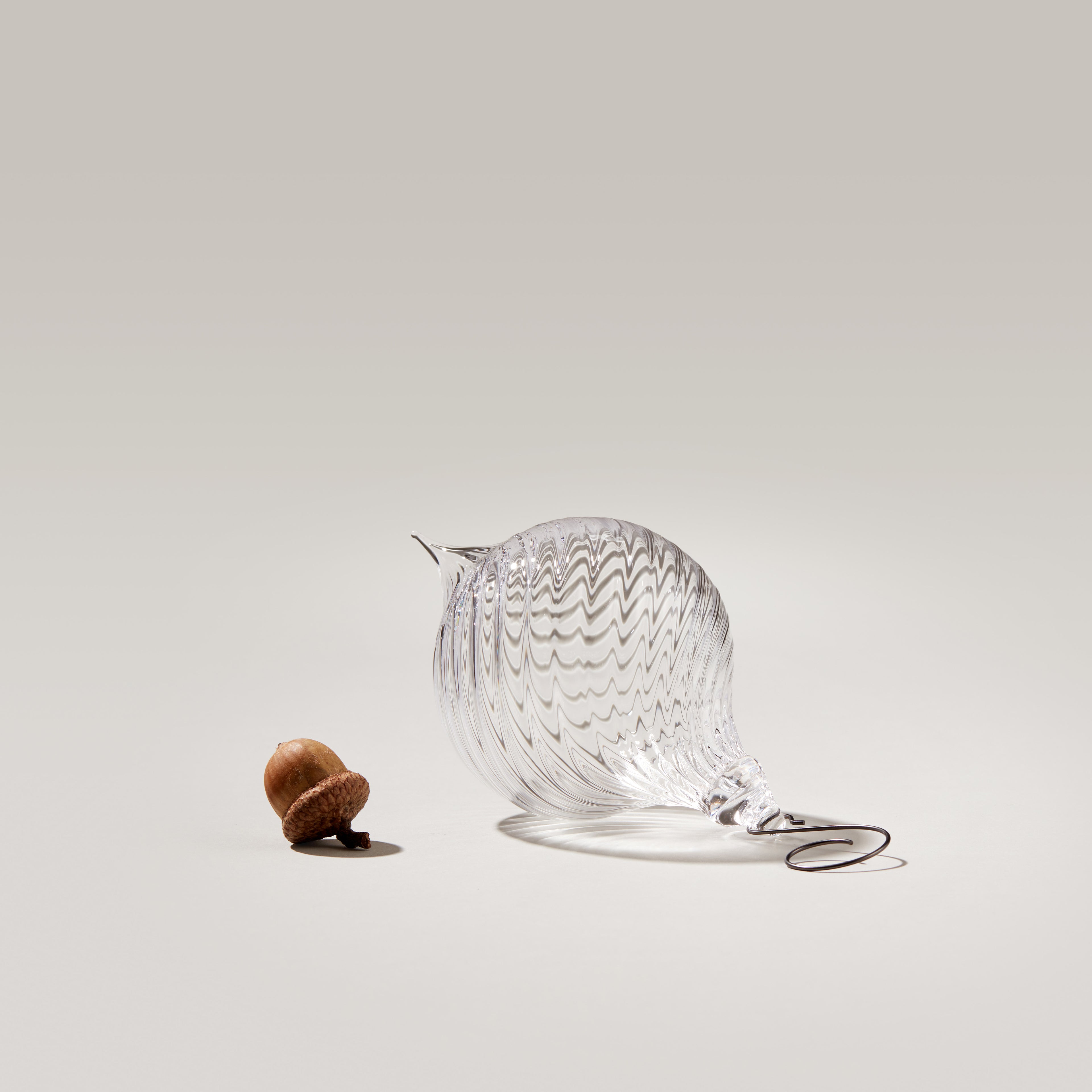 Clear glass finial ornament with optic ridged pattern and metal cap, shown next to walnut for scale.