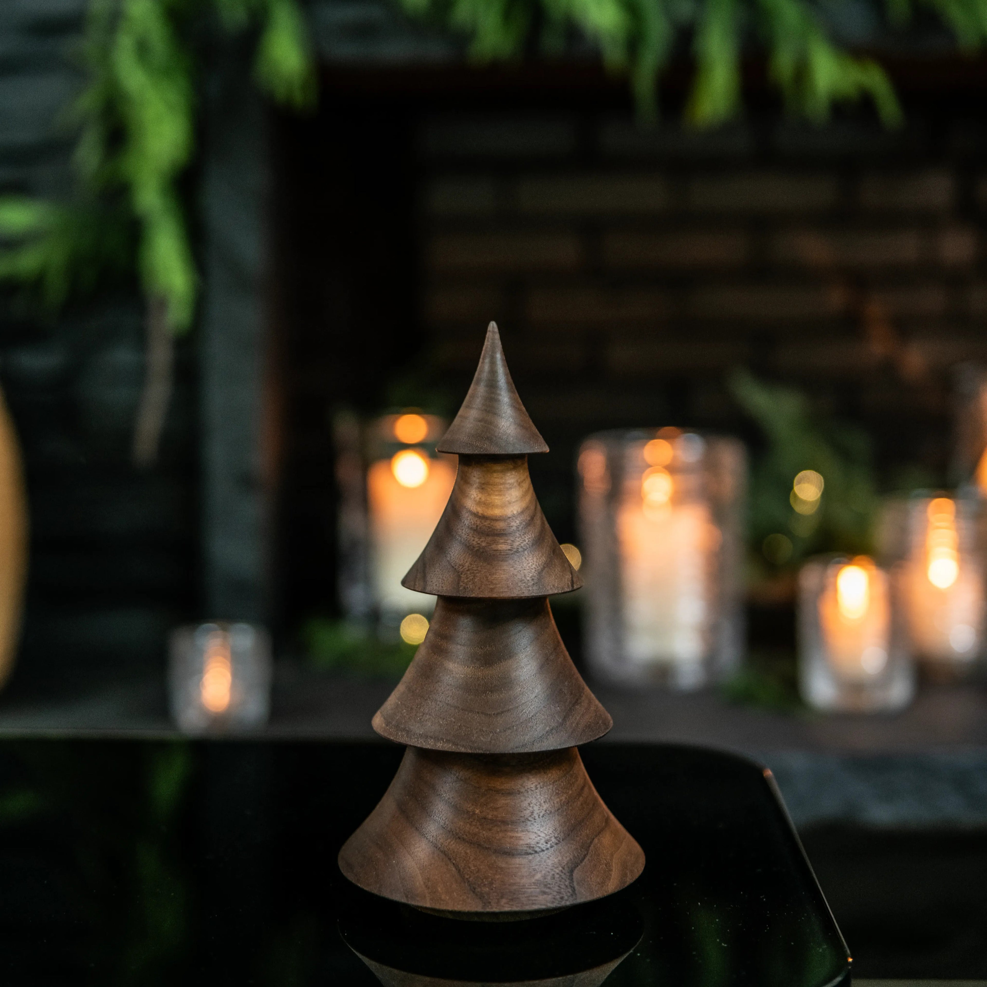 Stacked walnut wood cone-shaped tree decoration with pointed top, displayed with lit candles in background.
