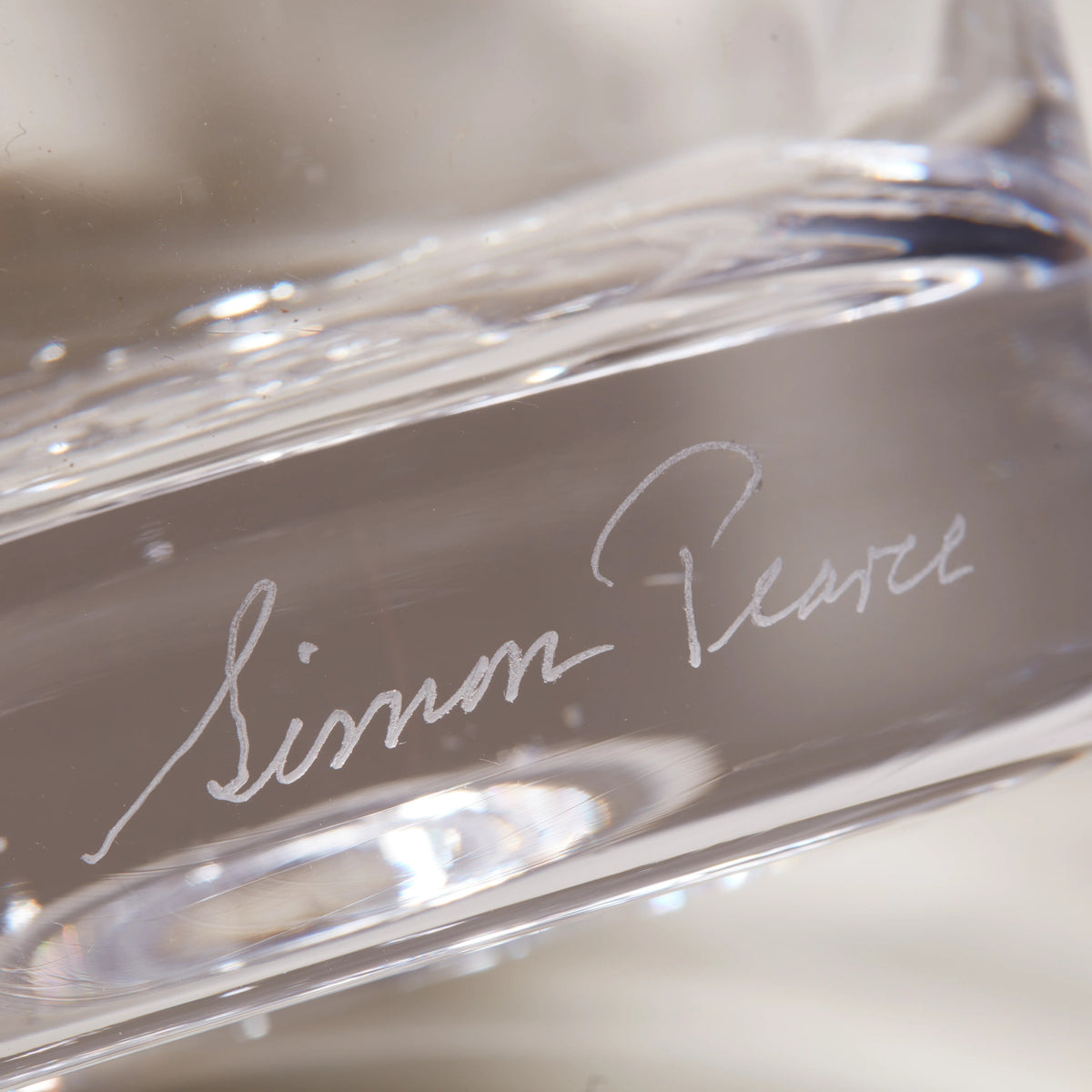 Clear glass vase with curved anemone-inspired form and artist signature etched on surface.