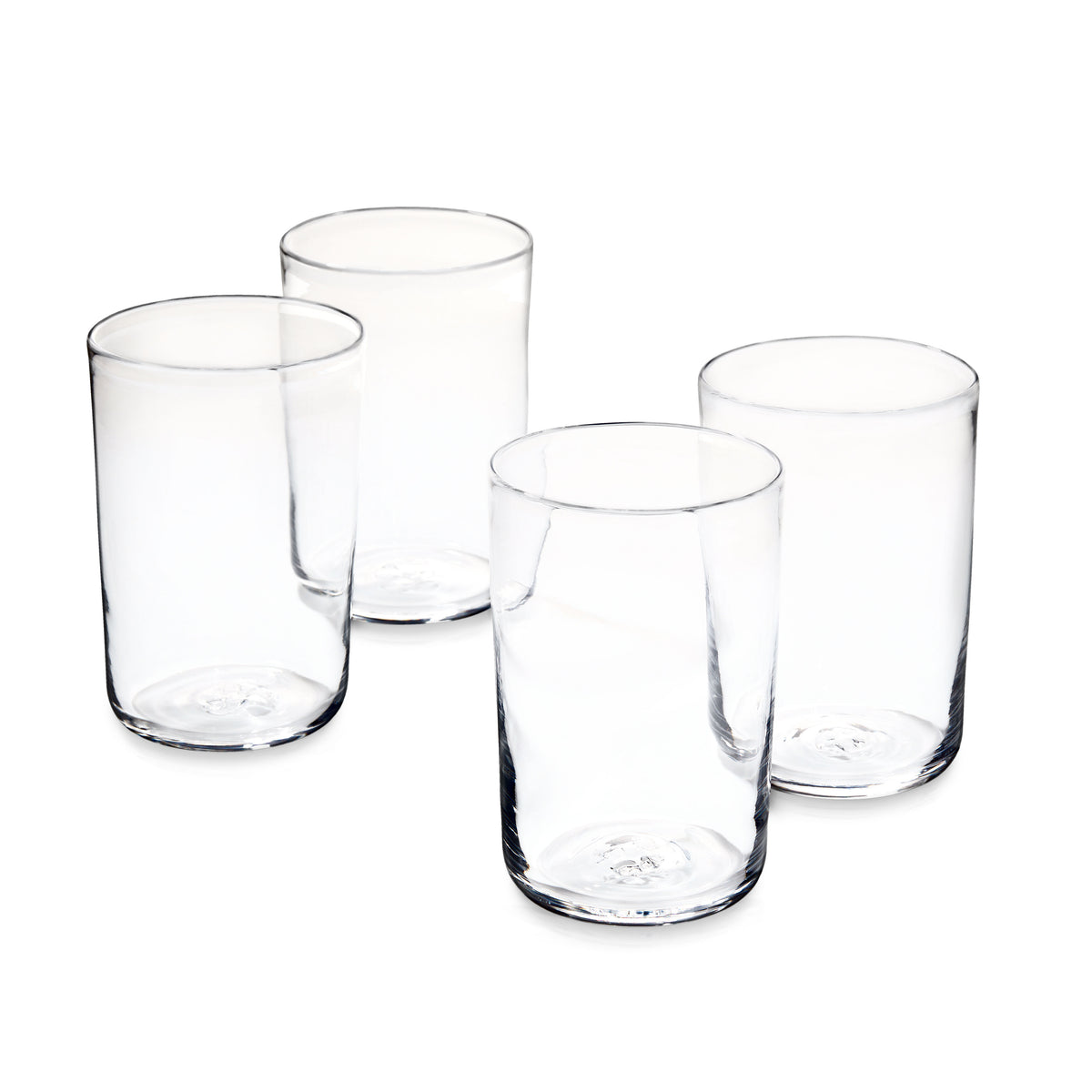 Four clear cylindrical drinking glasses with rounded rims arranged in a group on white background.