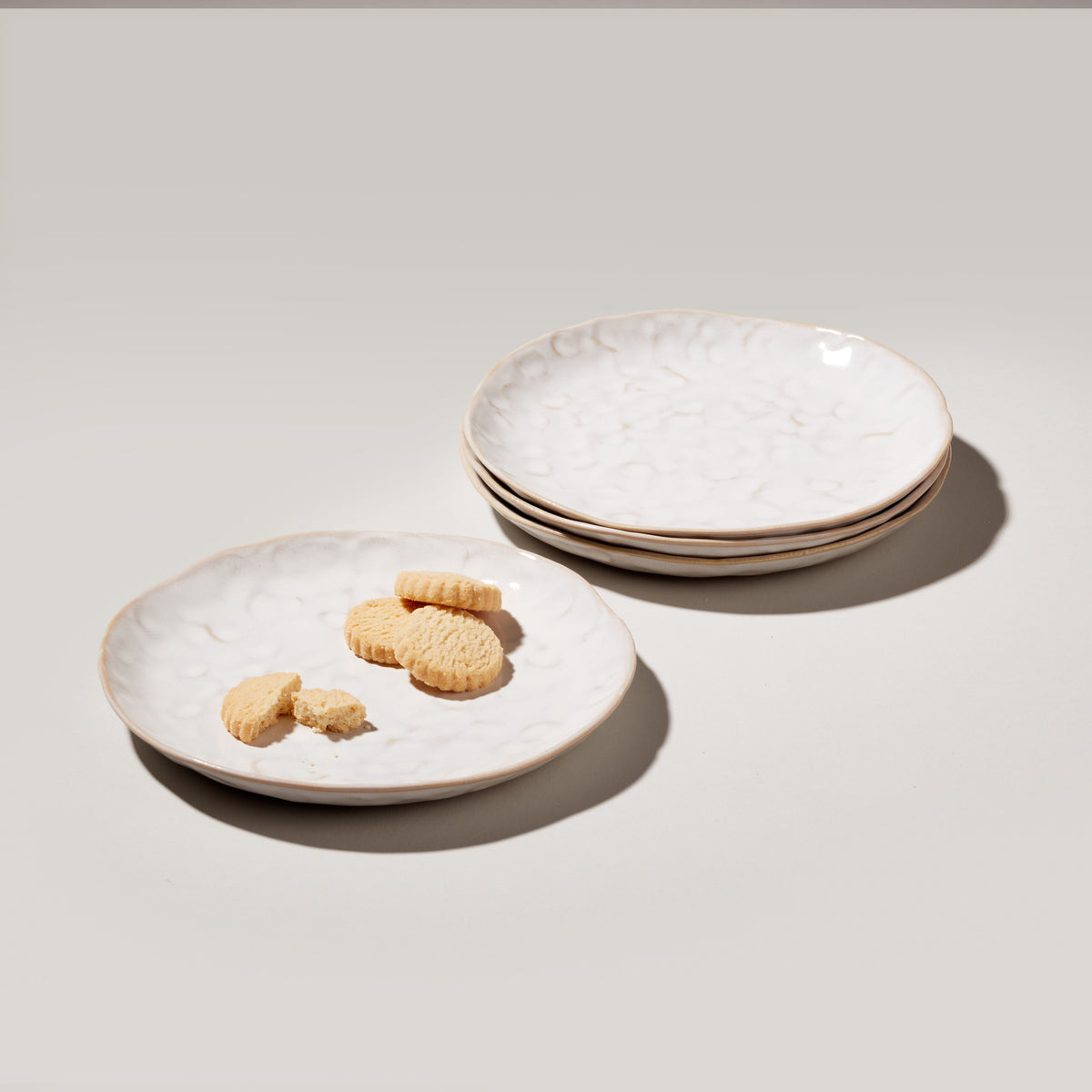 Four white appetizer plates with scalloped edges and gold-toned rims, one holding small crackers.