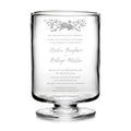 Clear hurricane glass with engraved wedding invitation text and floral design at top.