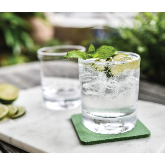 Clear cocktail glasses with ice, fresh lime slices, and mint leaves on green coasters, displayed on marble surface.