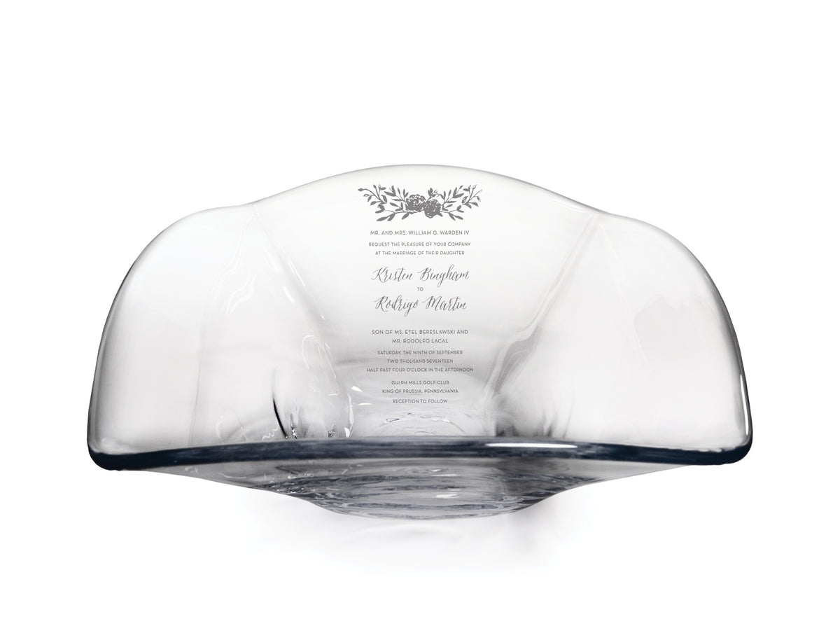 Large clear glass bowl with curved rim and engraved wedding invitation text and floral design on interior.