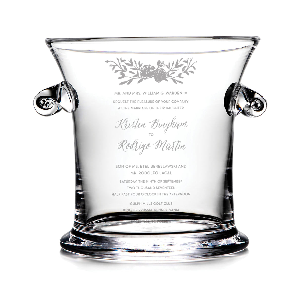 Clear glass ice bucket with engraved wedding invitation text and floral design, featuring two black handles.