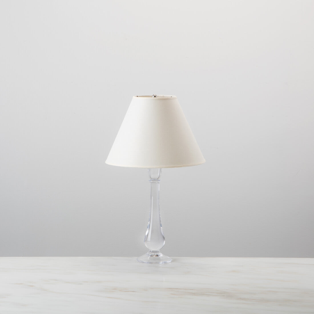Table lamp with clear glass teardrop base and cream linen tapered shade.
