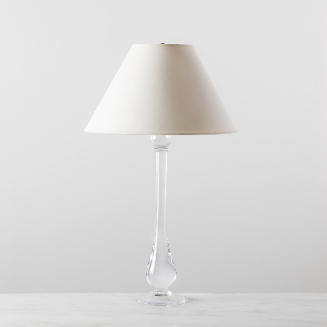 Tall table lamp with clear glass tapered stem and cream linen trapezoid shade.