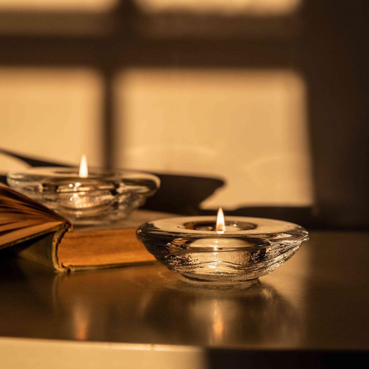 Two lit tealights in clear glass holders on a dark surface with warm ambient lighting.