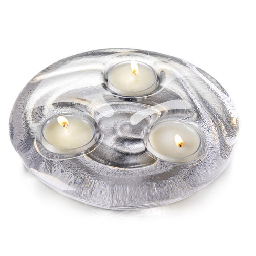 Three lit tealights in cream-colored cups set in a silver textured circular holder.