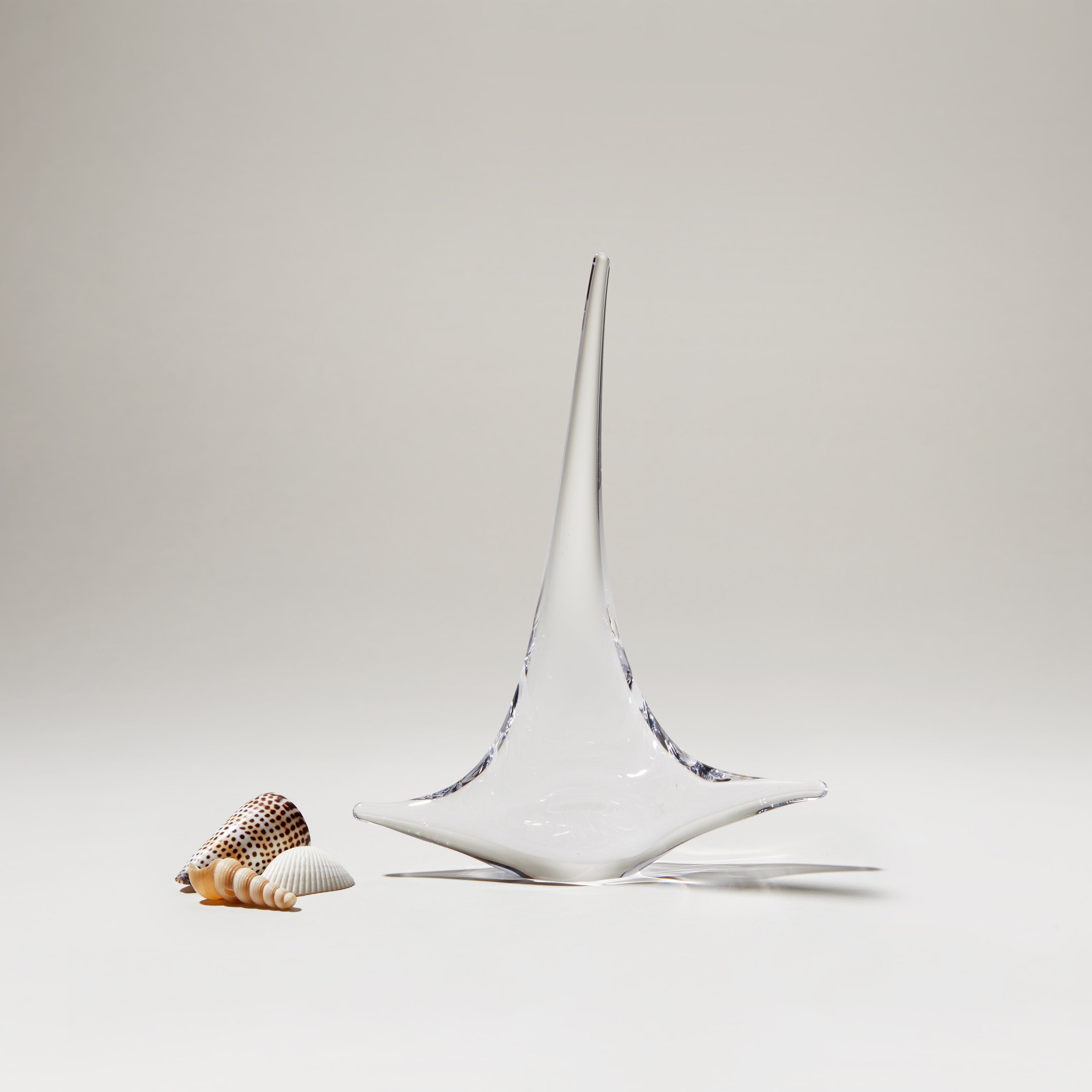 White ceramic sailboat with pointed mast and blue accents, displayed next to small shells on neutral background.