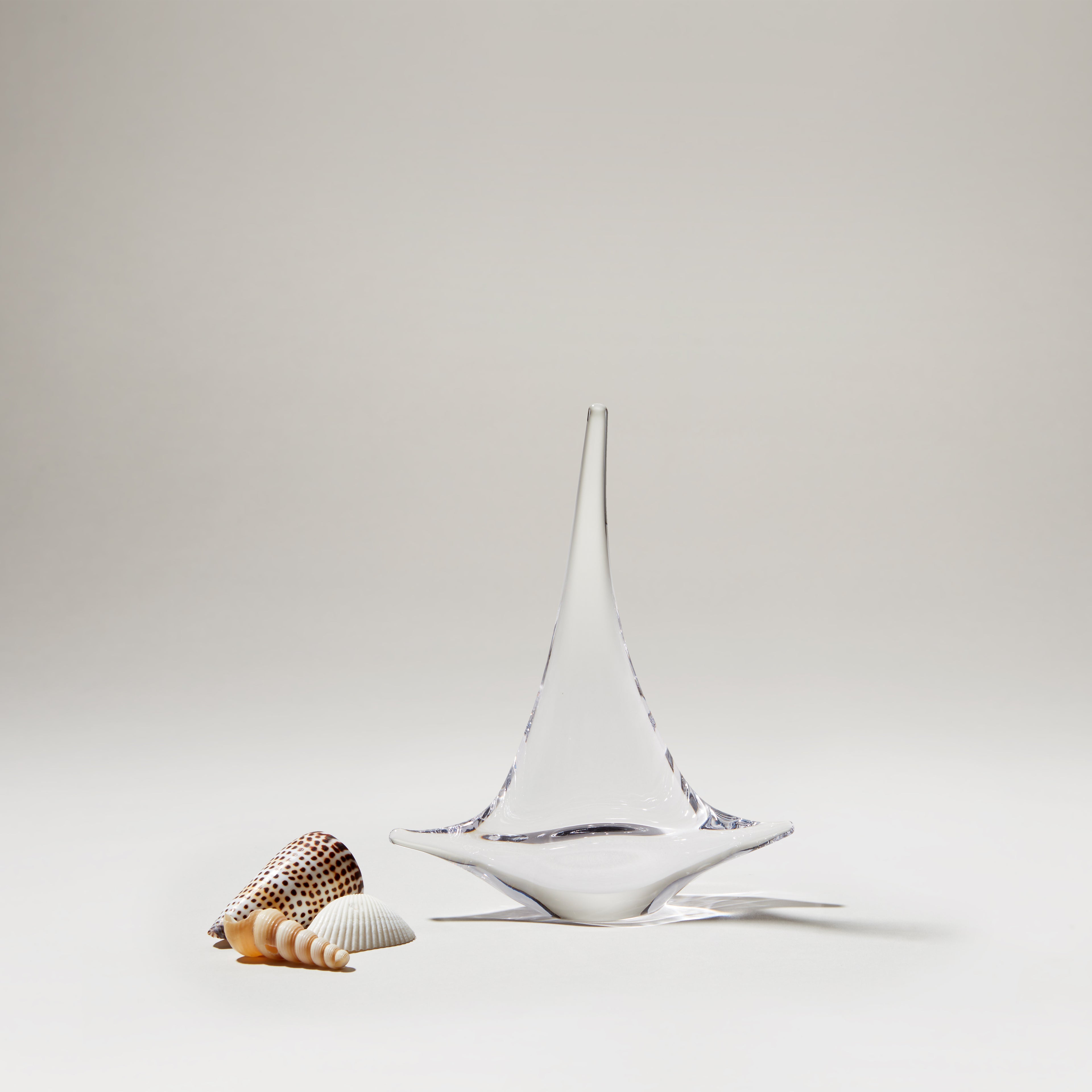 White ceramic sailboat with blue accents next to shells on neutral background.