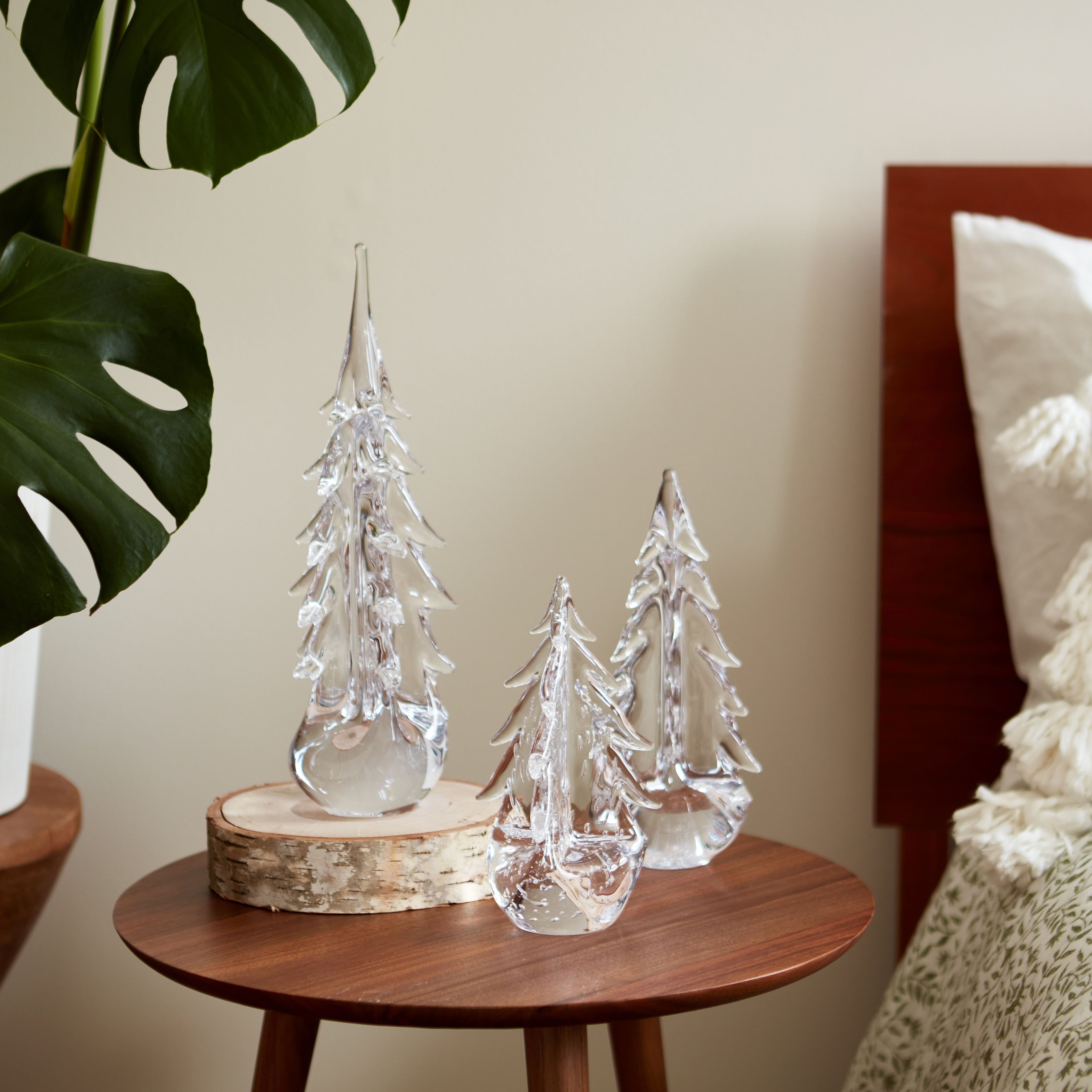 Clear glass evergreen trees of varying heights on wooden base with birch-wrapped accent piece.