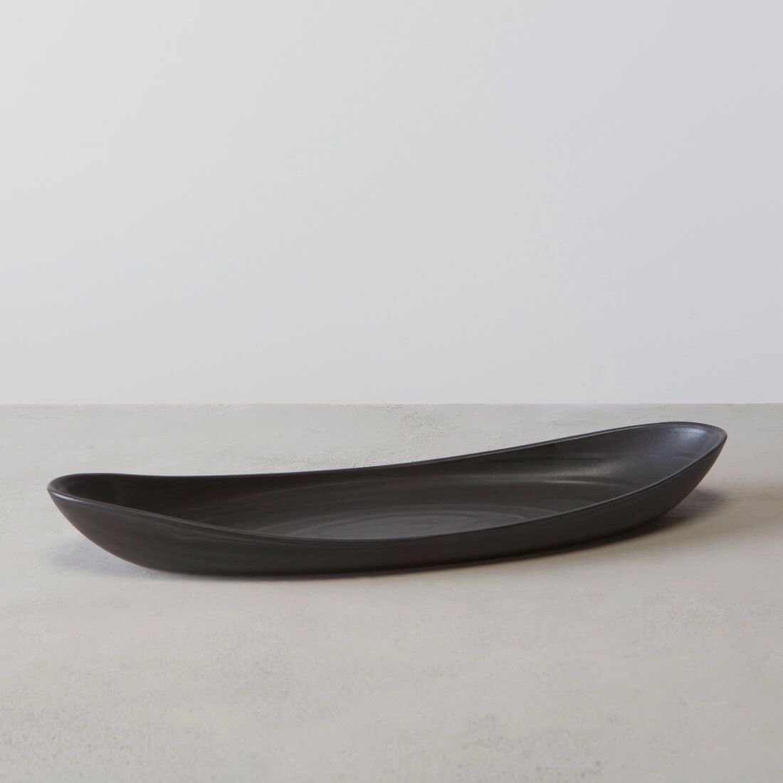Black elongated serving platter with curved edges and shallow well for holding food.