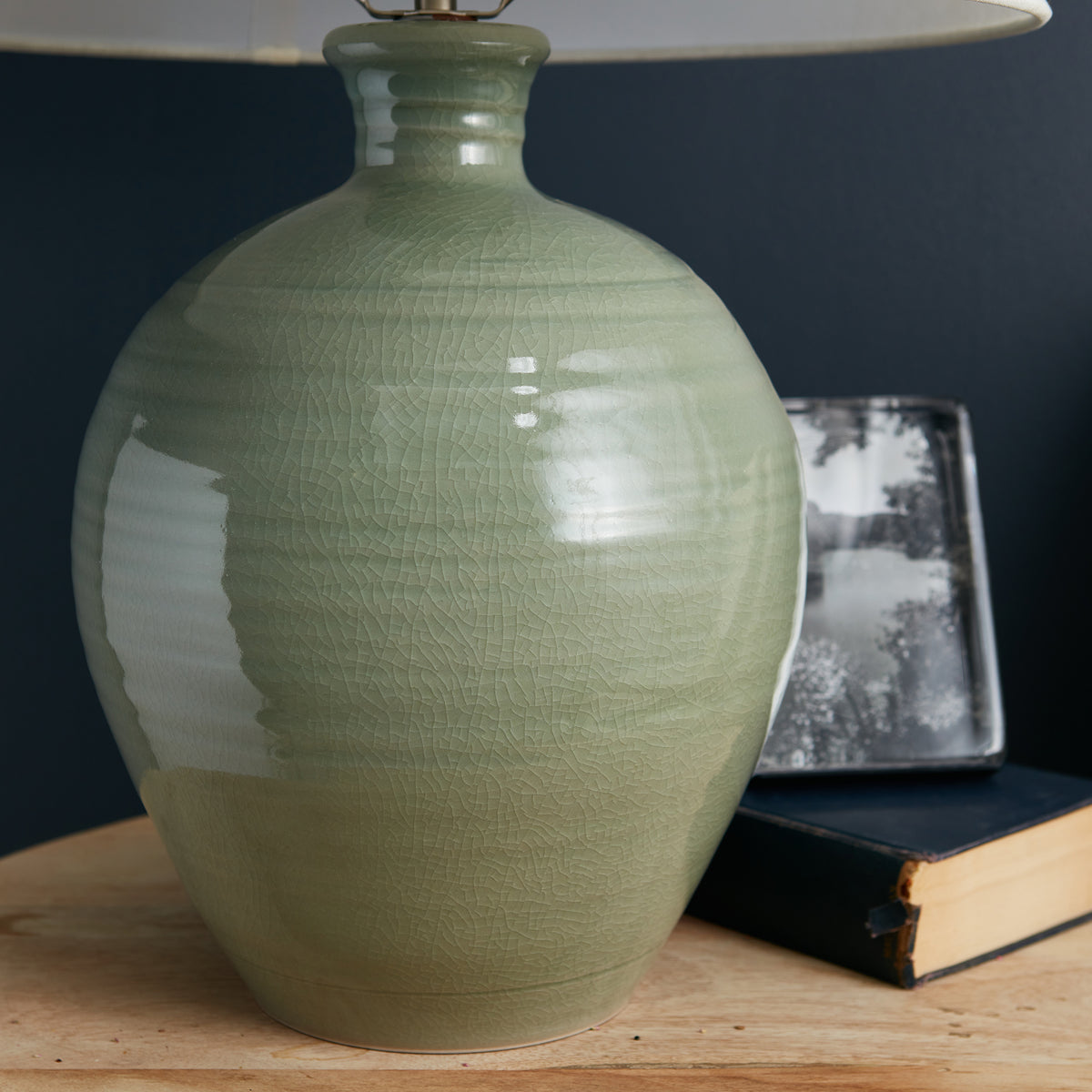 Sage green pottery lamp base with crackle glaze finish and cream linen shade on wooden surface.