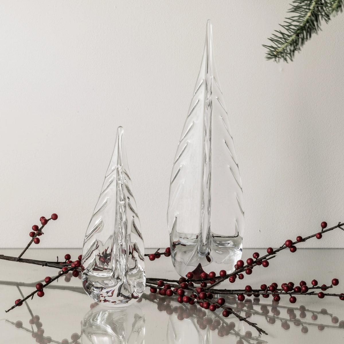 Clear glass tree-shaped decorations with textured surfaces, displayed with red berries and evergreen sprigs.