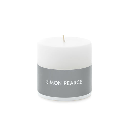 White cylindrical pillar candle with gray band labeled "SIMON PEARCE" and tan wick.