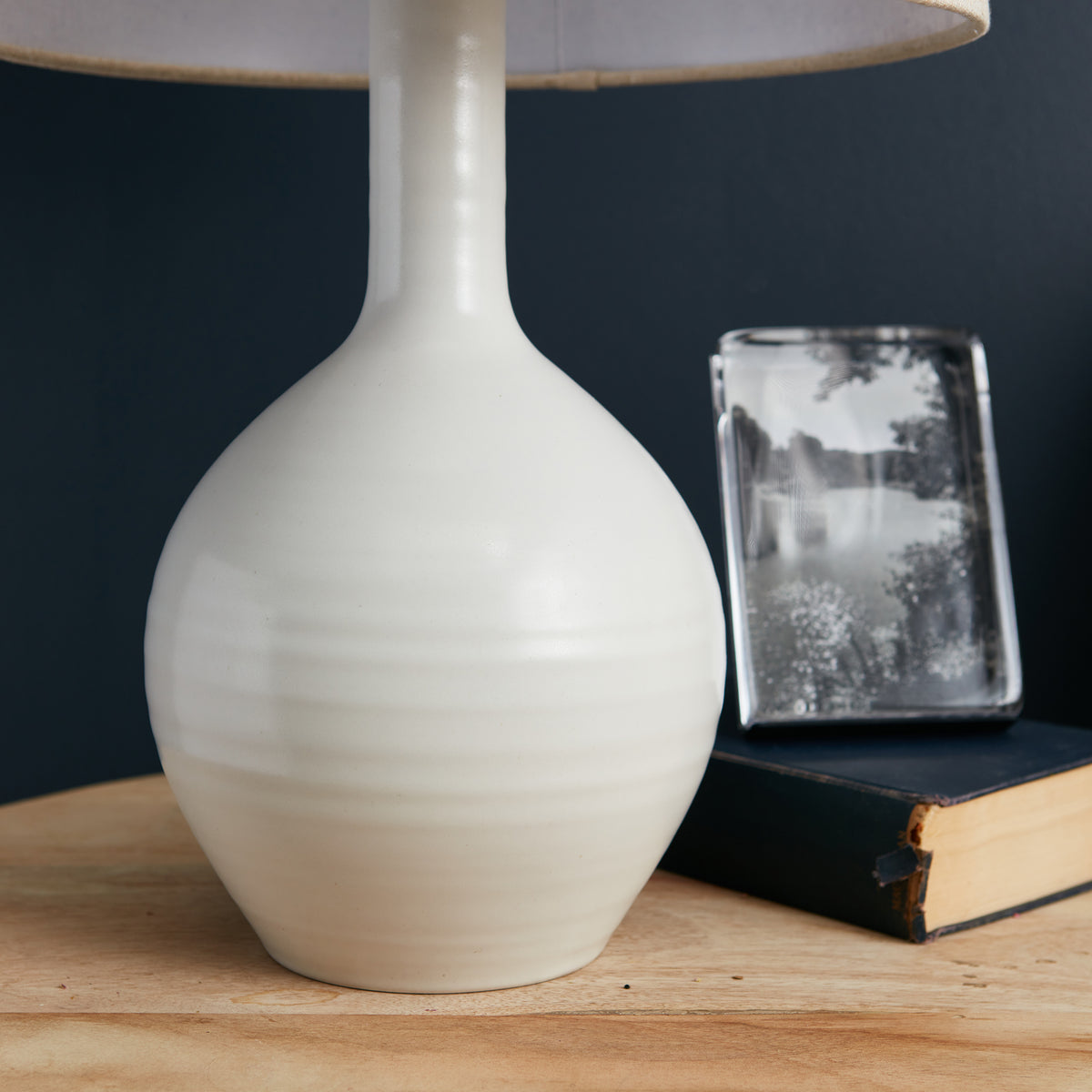 Small white ceramic table lamp with bulbous base, narrow neck, and tan linen shade.
