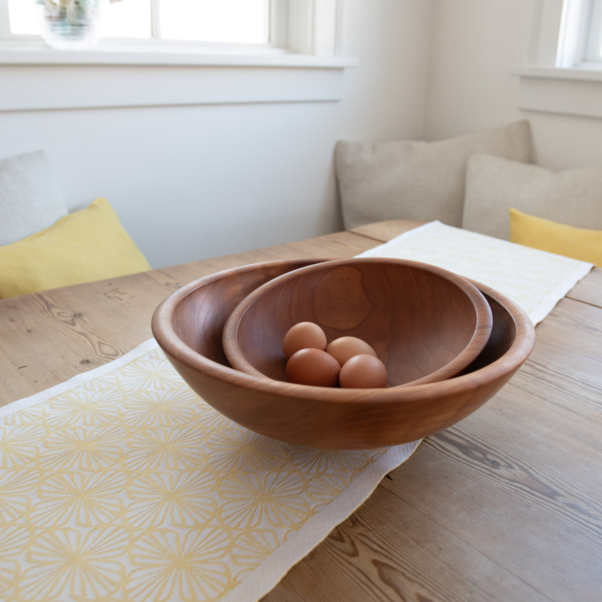 Cherry wood nesting bowls with rounded sides, containing brown eggs, displayed on a wooden table.