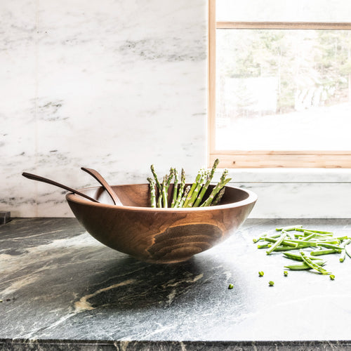 Dark wood bowl with two wooden spoons, containing fresh green beans on a marble countertop.
