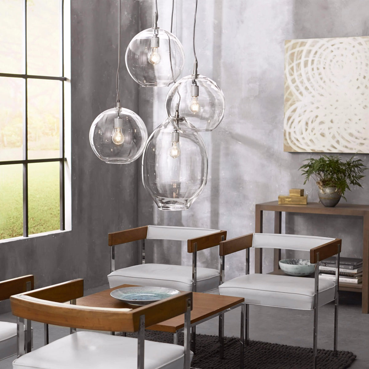 Four clear glass globe pendant lights with exposed bulbs hanging at varying heights above a dining table.
