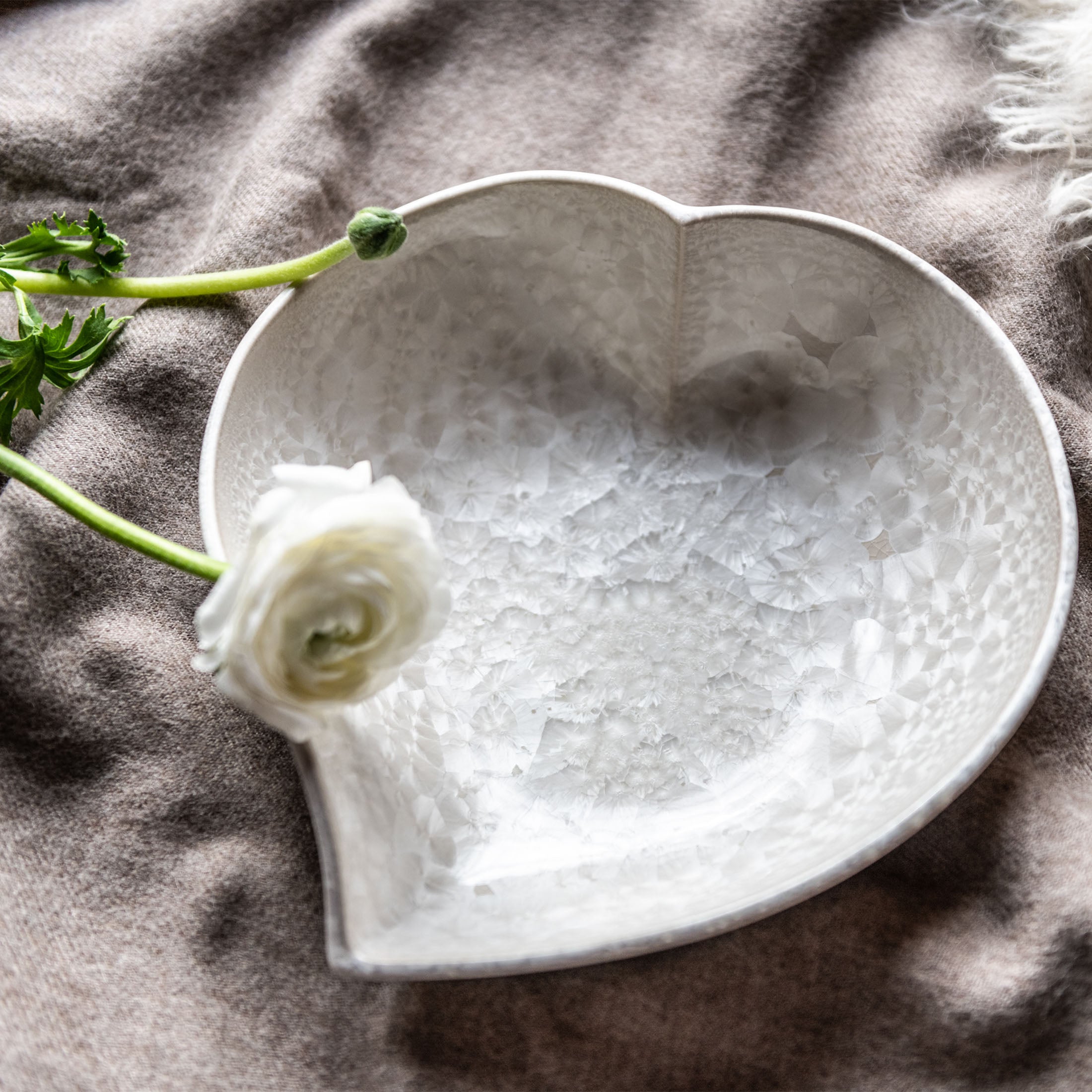 White ceramic heart-shaped bowl with textured interior surface, displayed on gray fabric with flowers.