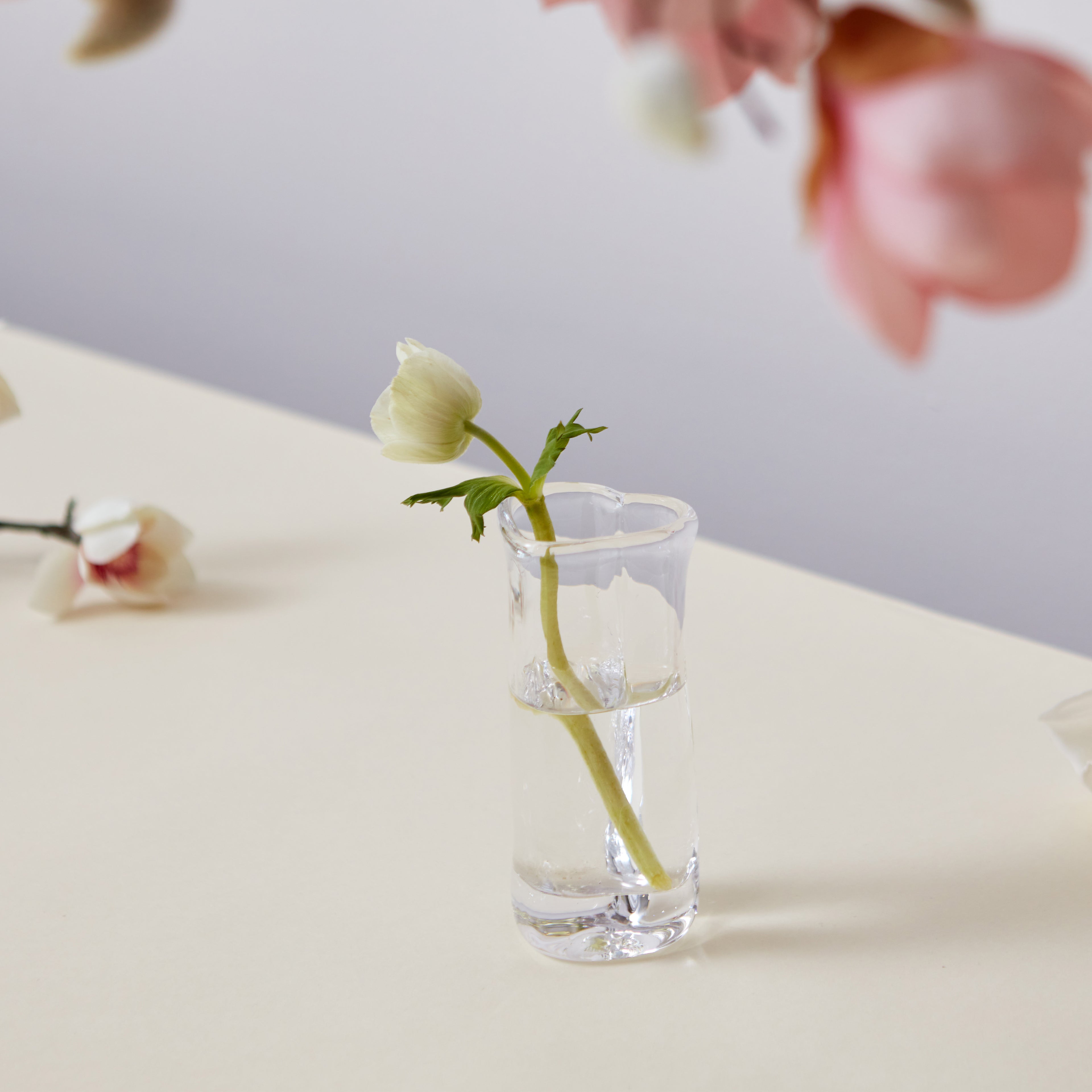 Clear glass heart-shaped bud vase holding a single pale yellow flower stem with water.