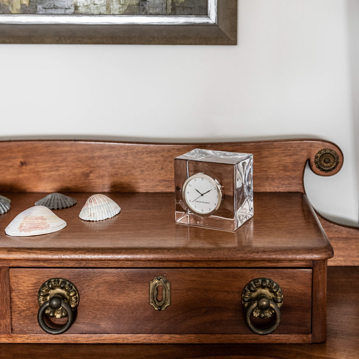 Clear crystal tabletop clock with white dial and dark hands, displayed on wooden furniture.