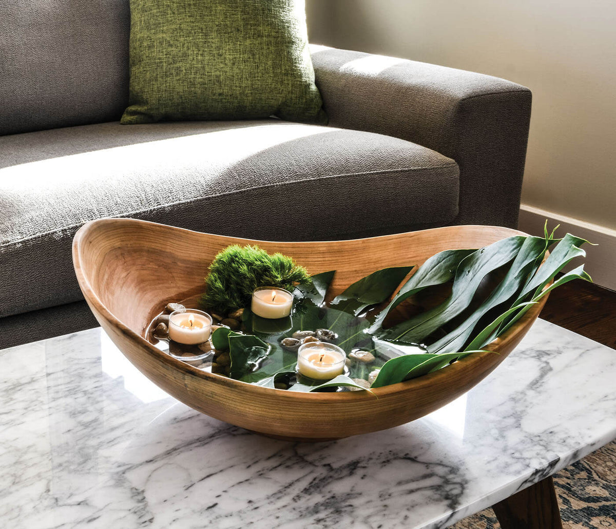 Cherry wood bowl with irregular live edge, containing candles and plant leaves, displayed on marble table.