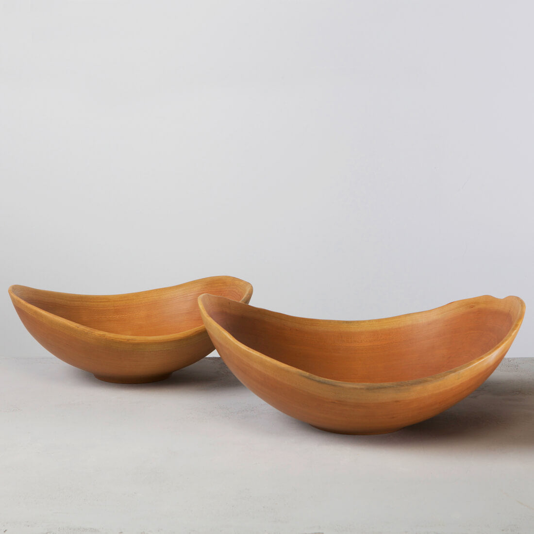 Two wooden bowls with natural live edges in warm cherry wood tones, curved oval shapes.