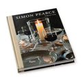 Hardcover book with black dust jacket featuring glassware, a lit candle, and place settings on the cover.