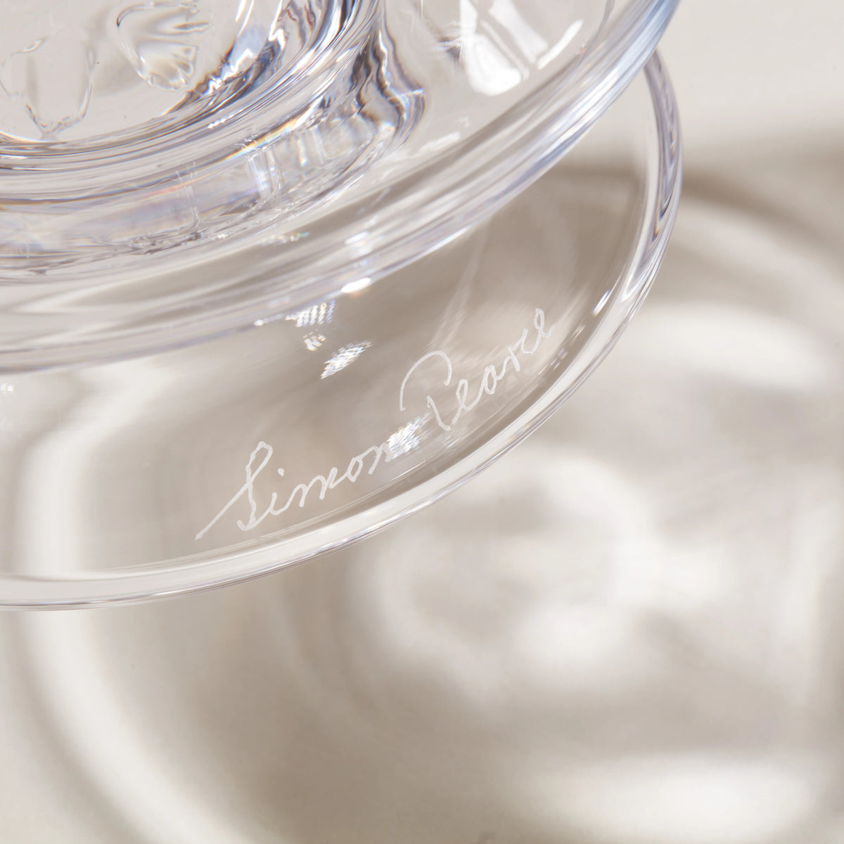 Clear glass hurricane lamp with engraved signature on base, shown in close-up detail.