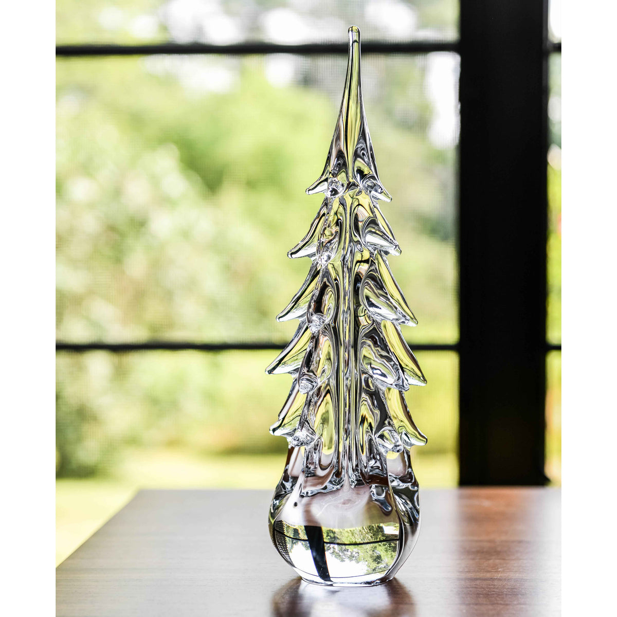 Clear glass tree-shaped figurine with pointed leaves and water-filled base, displayed on a wooden table.