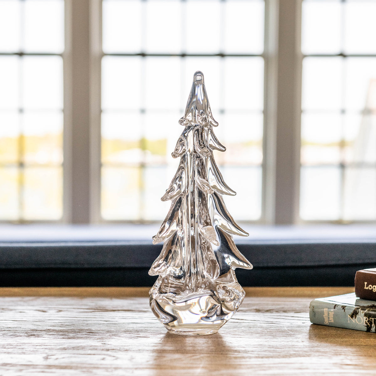 Clear glass evergreen tree decoration with tiered branches and pointed top sitting on wooden surface.
