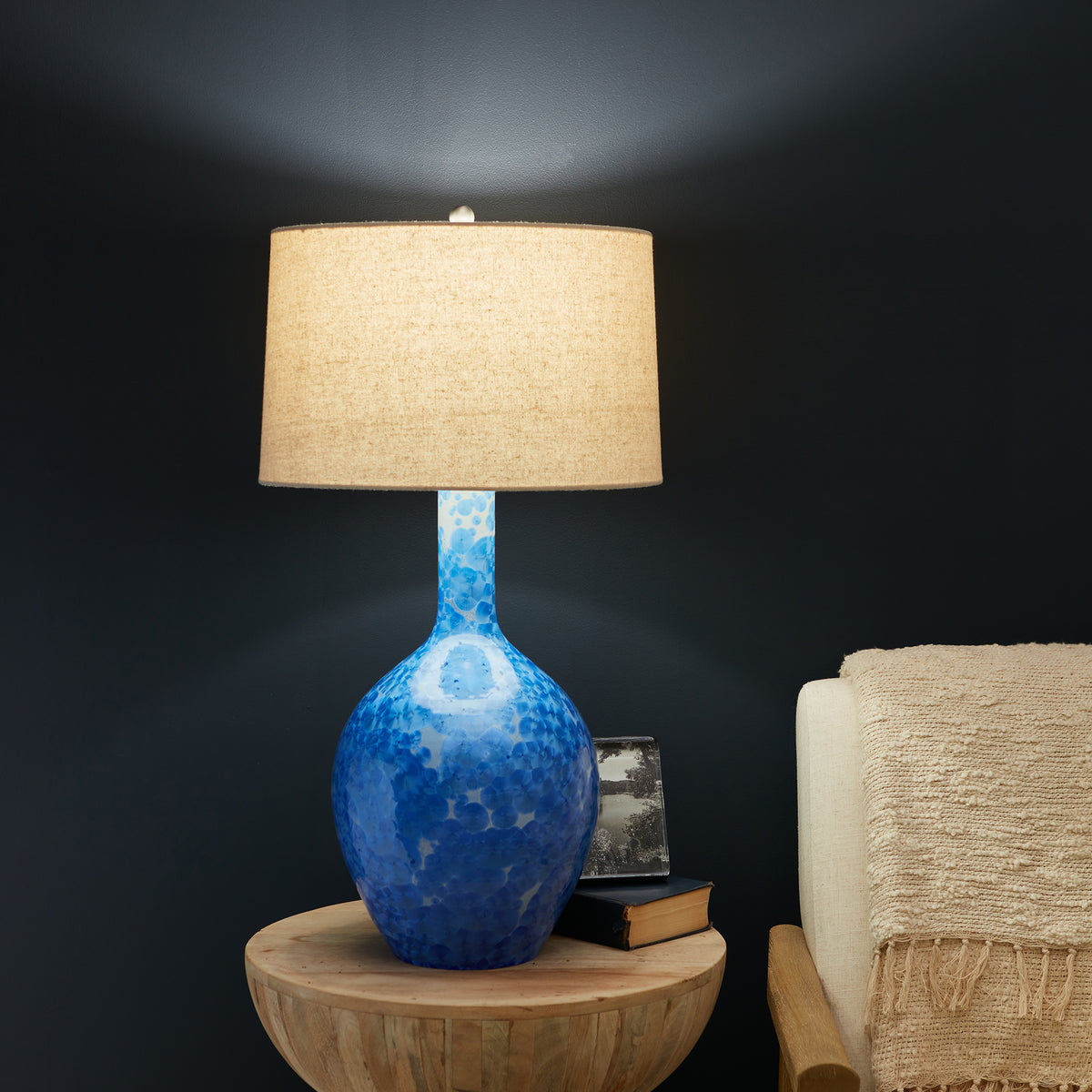 Blue crystalline ceramic base lamp with beige linen cylindrical shade on wooden table.