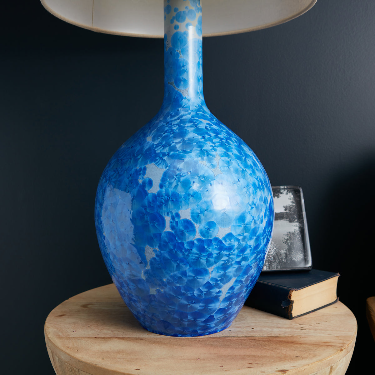 Blue and white crystalline patterned lamp base with tapered neck and cream linen shade on wooden table.