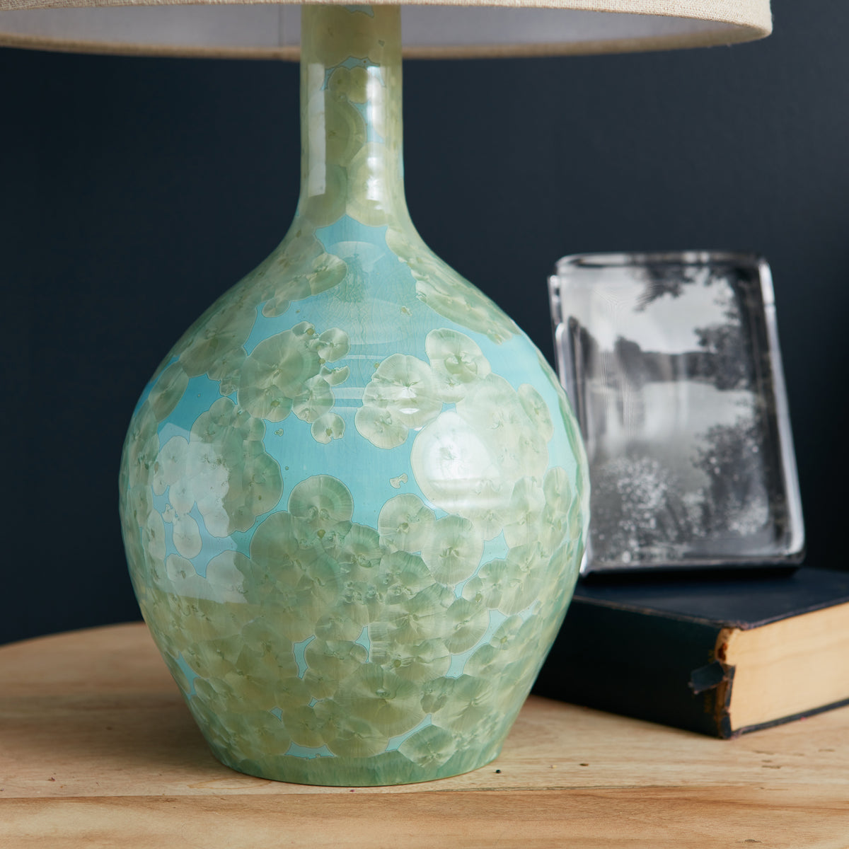 Green and blue crystalline lamp base with cream linen shade, displayed with decorative objects.