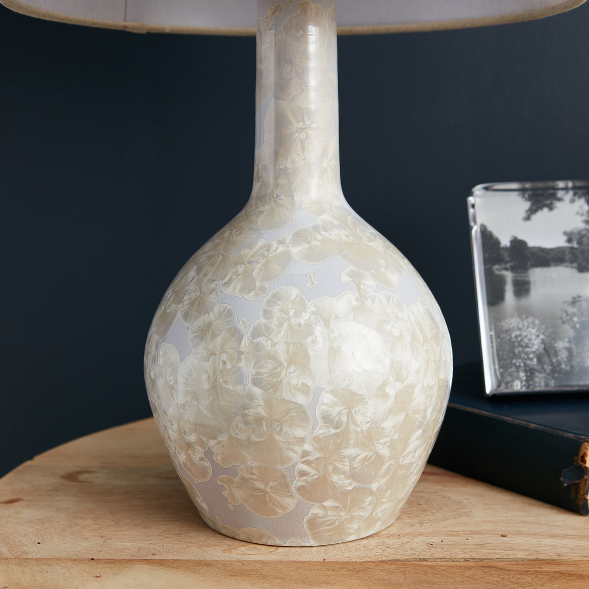 Cream-colored crystalline table lamp with carved floral relief pattern and fabric shade on wooden base.