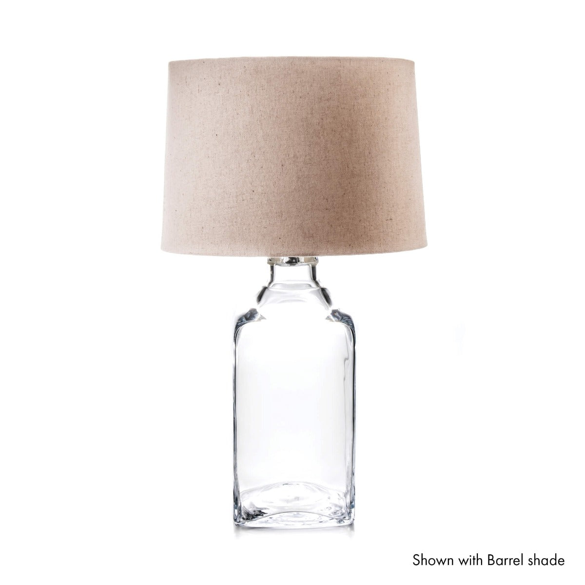 Clear glass bottle table lamp with beige linen cylindrical shade.