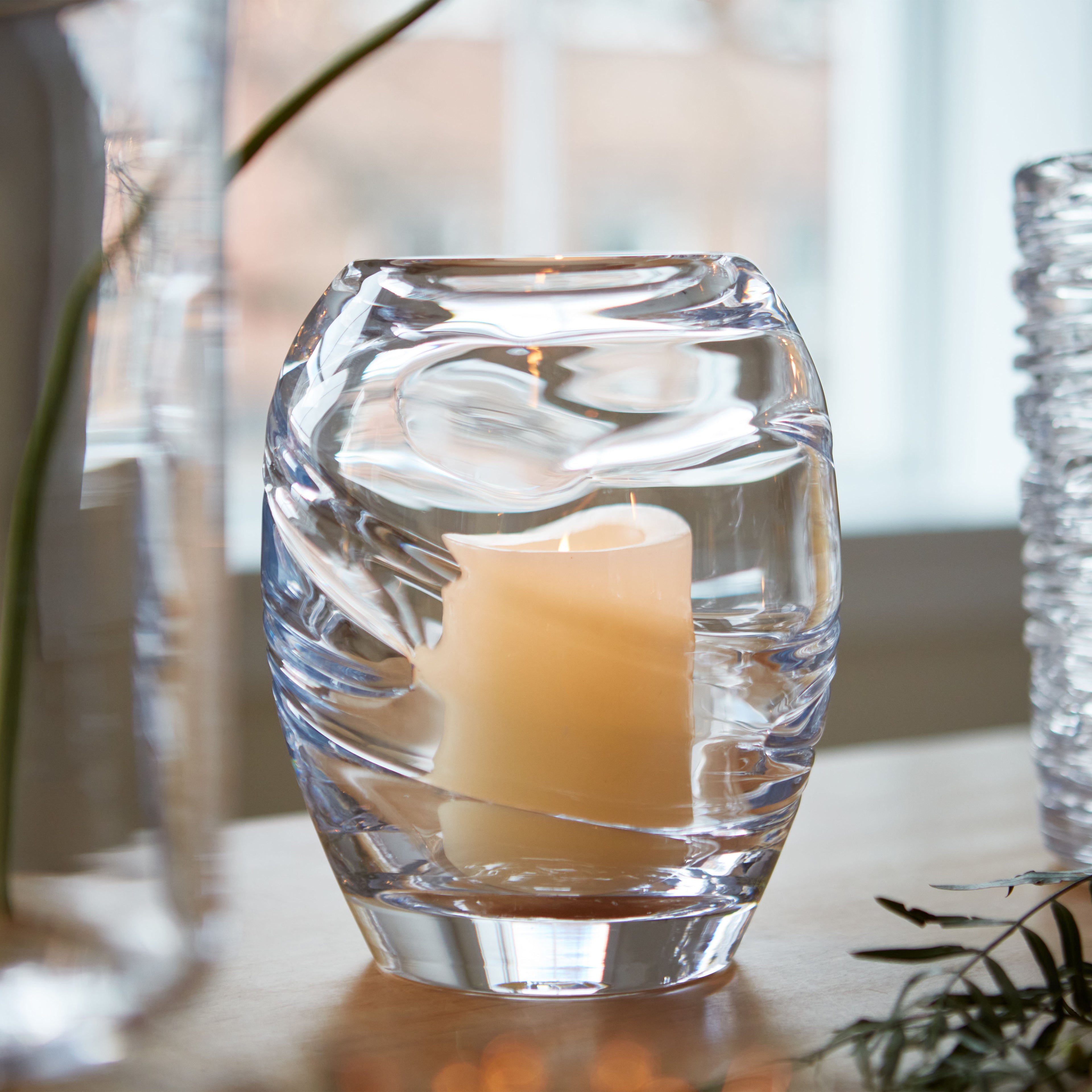 Clear glass hurricane vase with swirled pattern containing a cream-colored pillar candle.