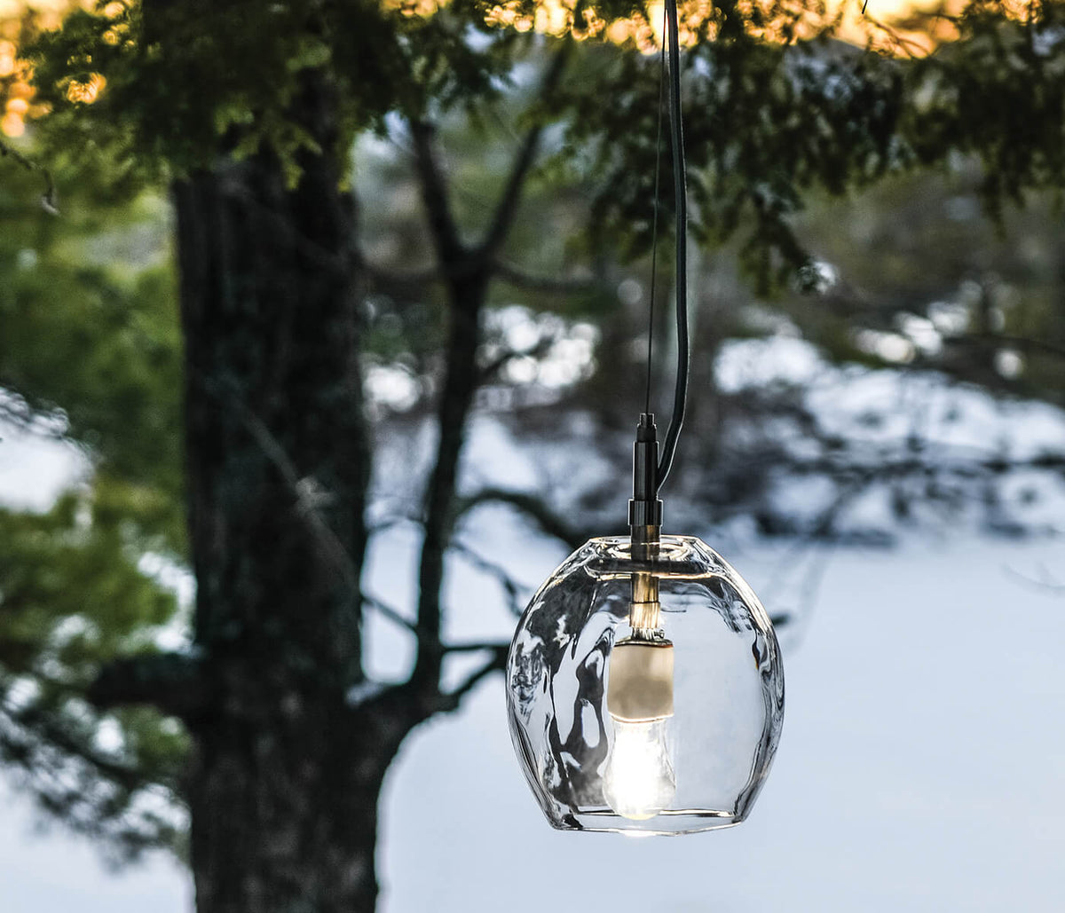 Clear glass globe pendant with textured surface suspended from black cord with brass hardware.