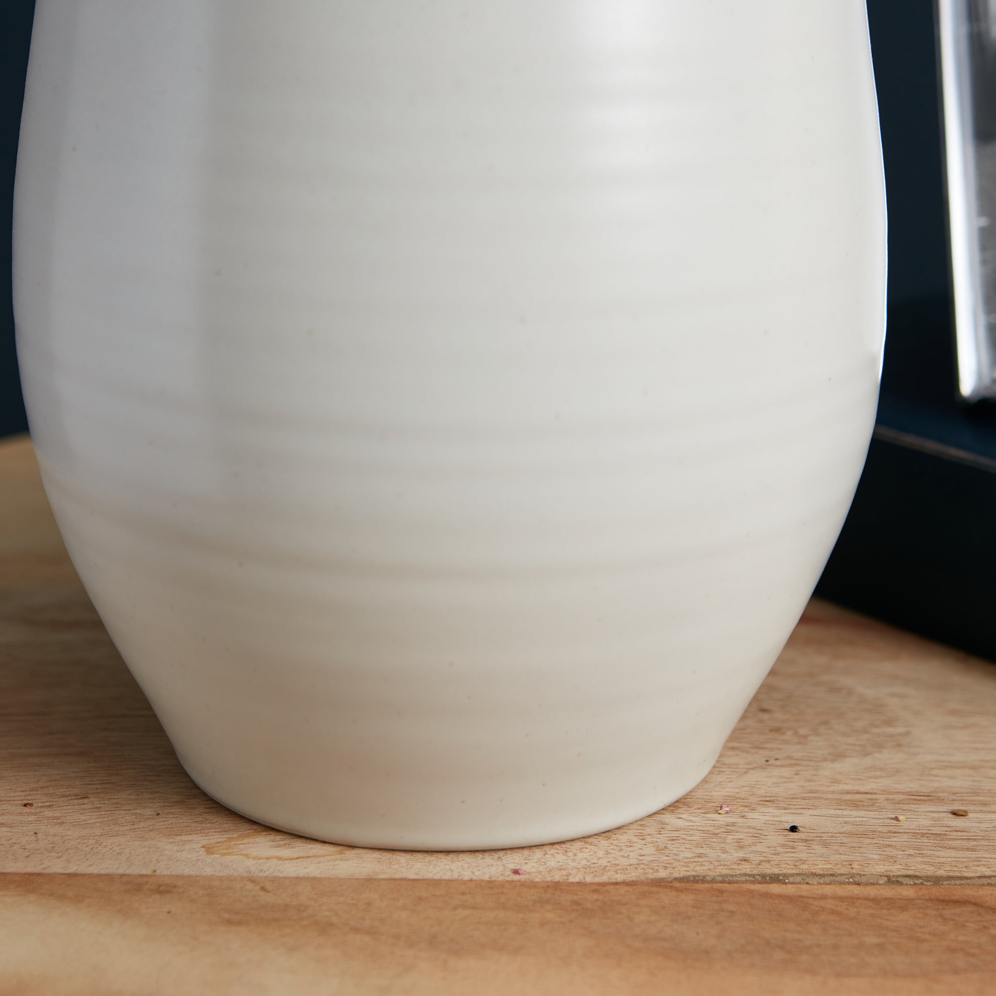 Cream-colored ceramic lamp base with rounded, tapered silhouette on wooden surface.